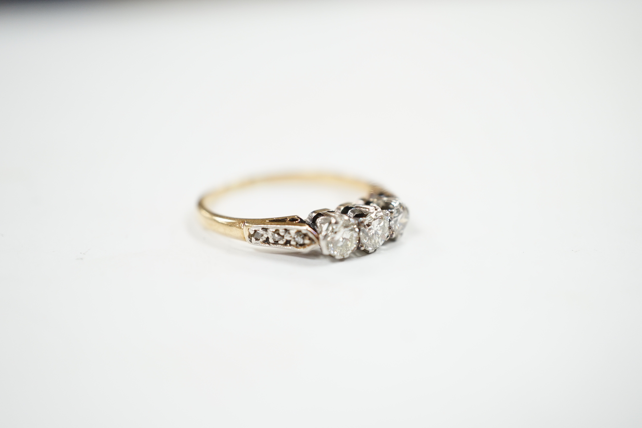 A yellow metal and three stone diamond set ring, with six stone diamond chip set shoulders, size L, gross weight 2.2 grams.
